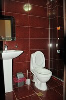 Un baño con paredes de azulejos rojos, un lavamanos blanco y un inodoro.