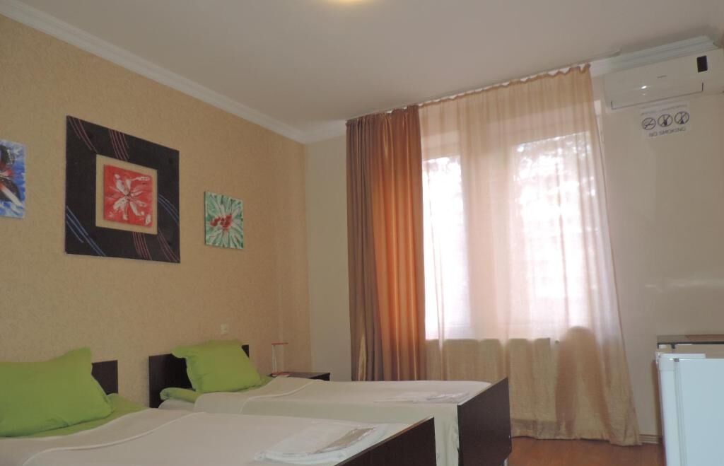 A hotel room with two beds, a refrigerator, and a window with curtains.