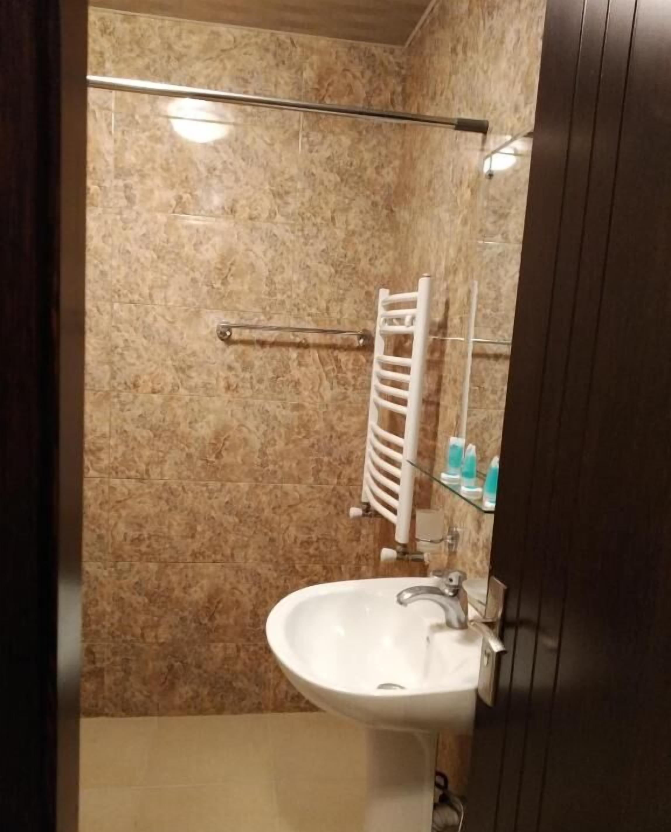 Un baño con pared de mármol, un lavamanos blanco y cabina de ducha de vidrio.