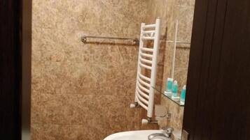 Un baño con pared de mármol, un lavamanos blanco y cabina de ducha de vidrio.