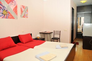 Comfortable room with a large bed, table, and chair, featuring two paintings and a refrigerator.