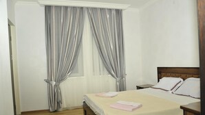 A hotel room with a bed, a nightstand, and a window with curtains. - Alma-Ata Hotel (Borjomi)