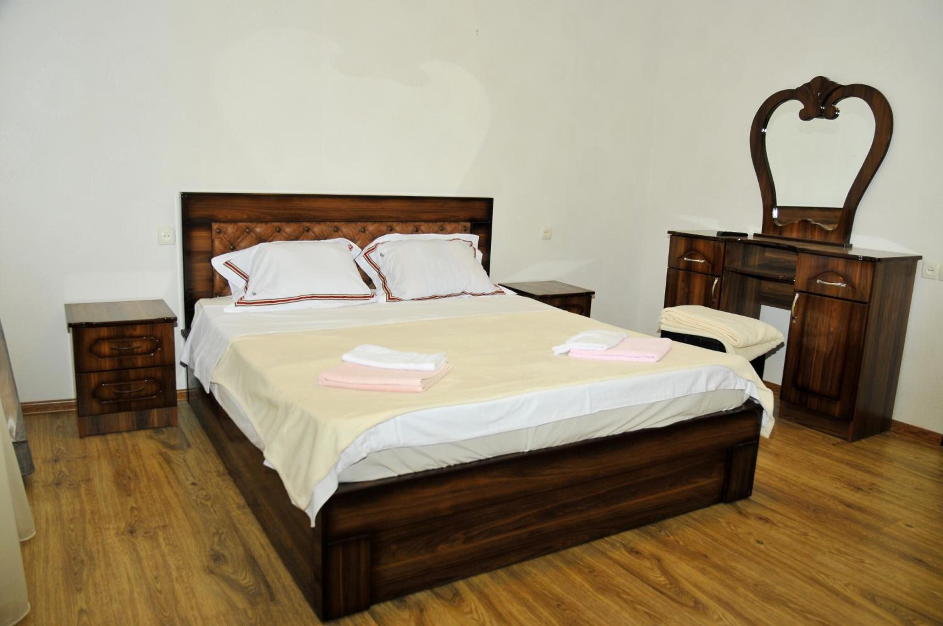 A bedroom with a wooden bed, two bedside tables, a dresser with a mirror, and a wooden floor.