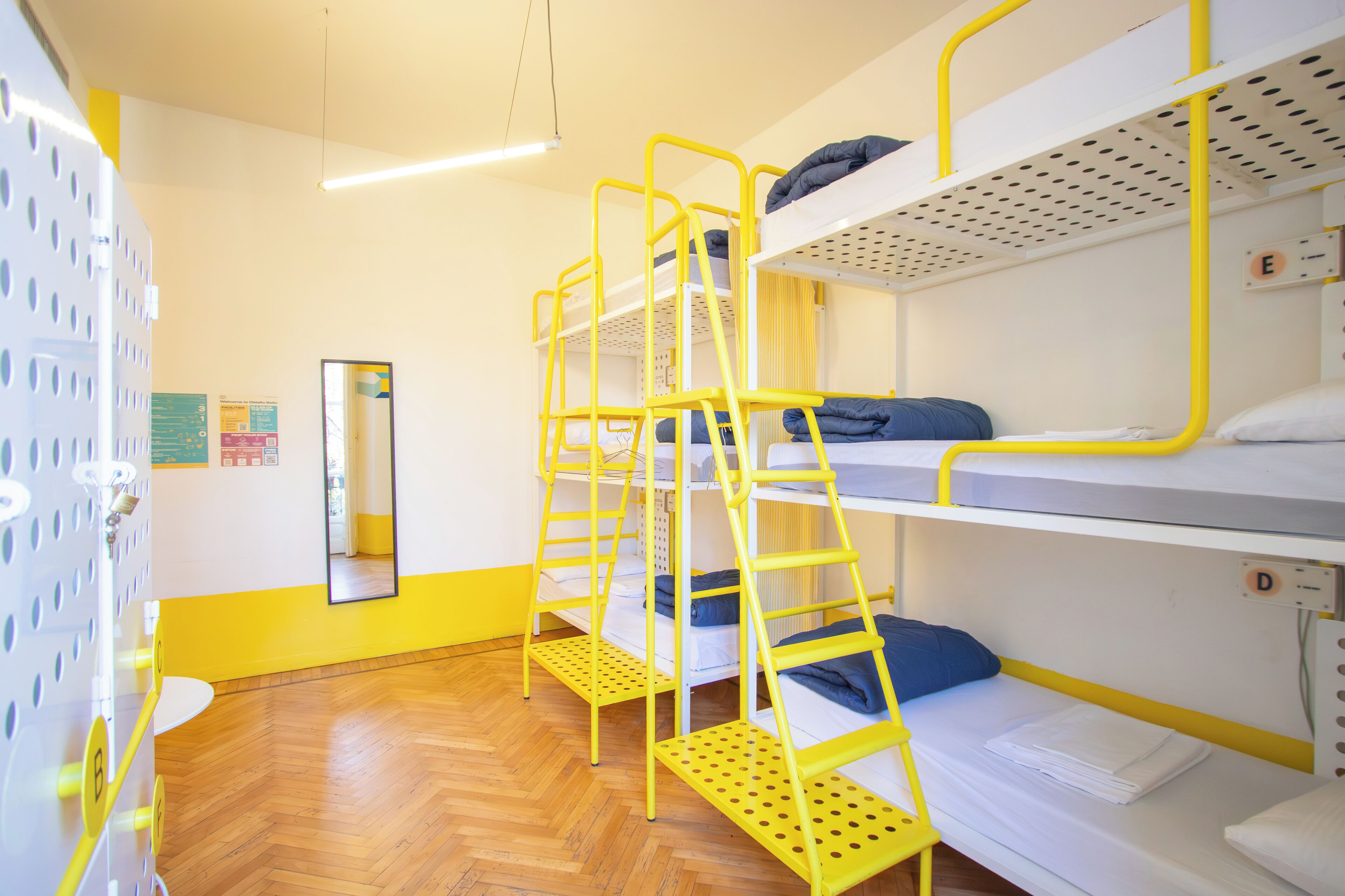 Quarto com beliches, escadas amarelas e roupa de cama branca.