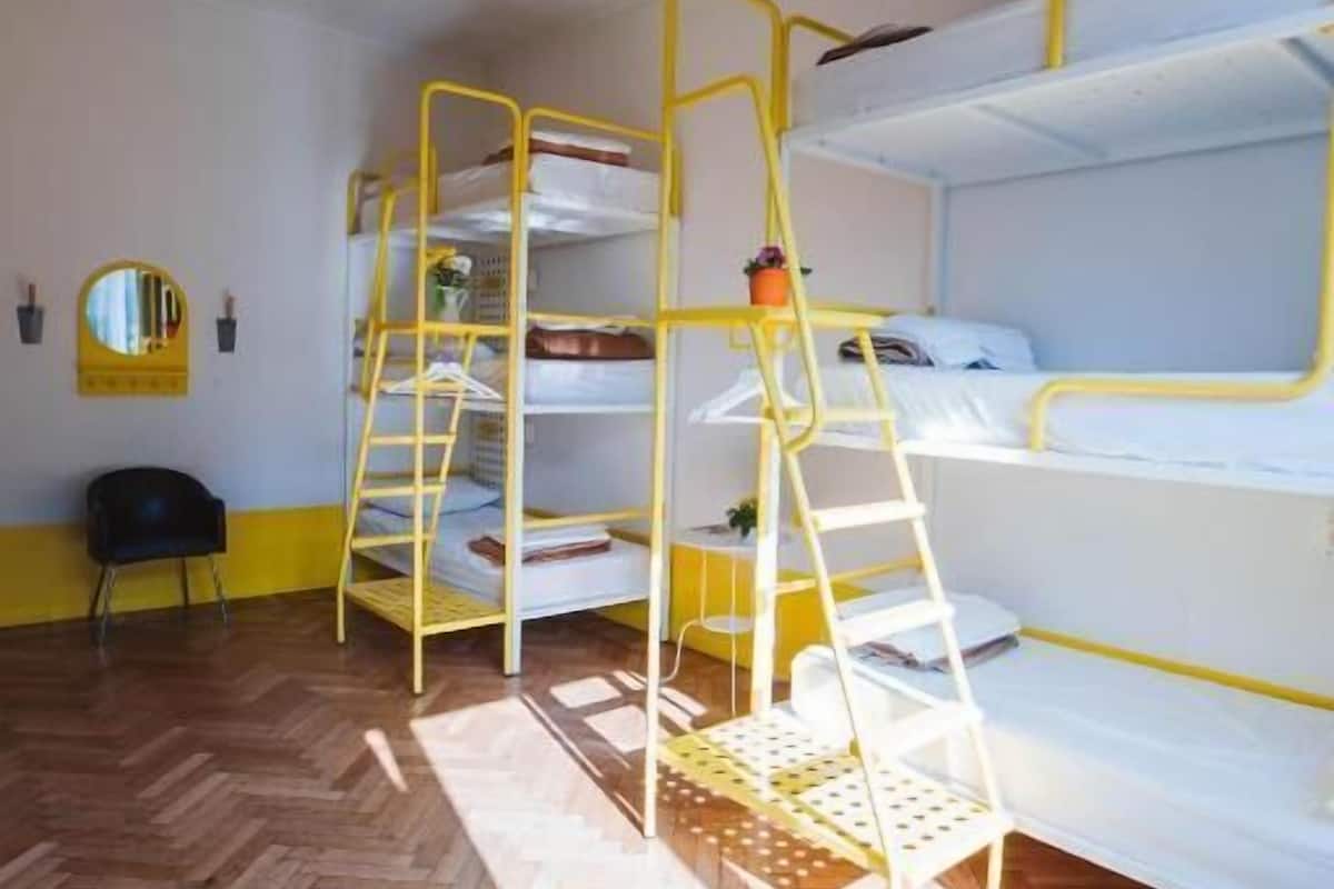 A room with bunk beds, a chair, a mirror, and a herringbone-patterned floor.