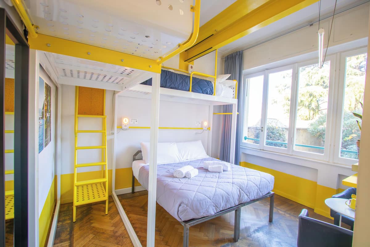 A bunk bed room with a ladder, a bed with pillows and towels, a small table, and a window with a view.