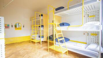 Un dormitorio con literas, suelo de madera y pared blanca con espejo y tablón de anuncios.