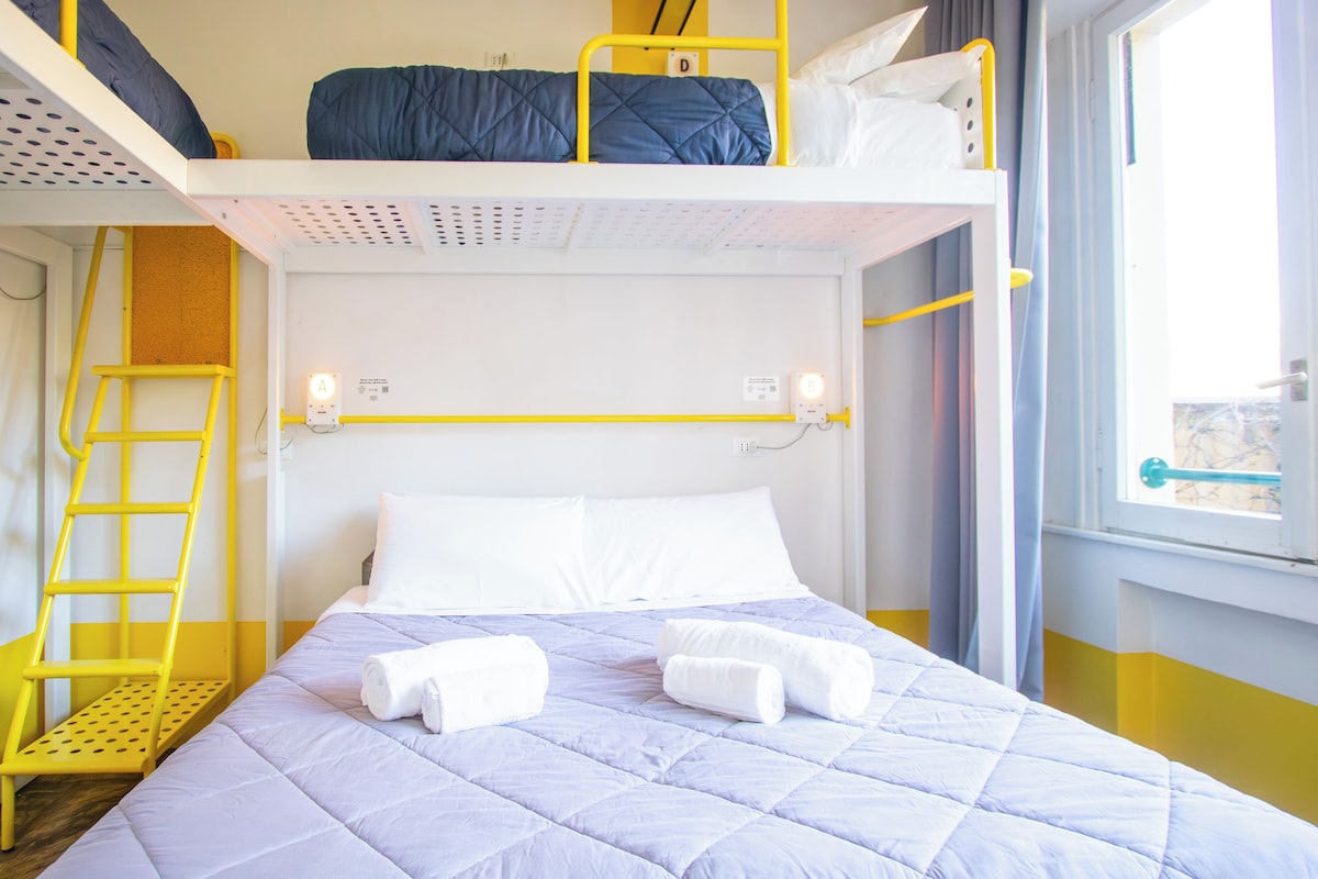 A bunk bed room with a ladder, a bed with white pillows, and a window with curtains.