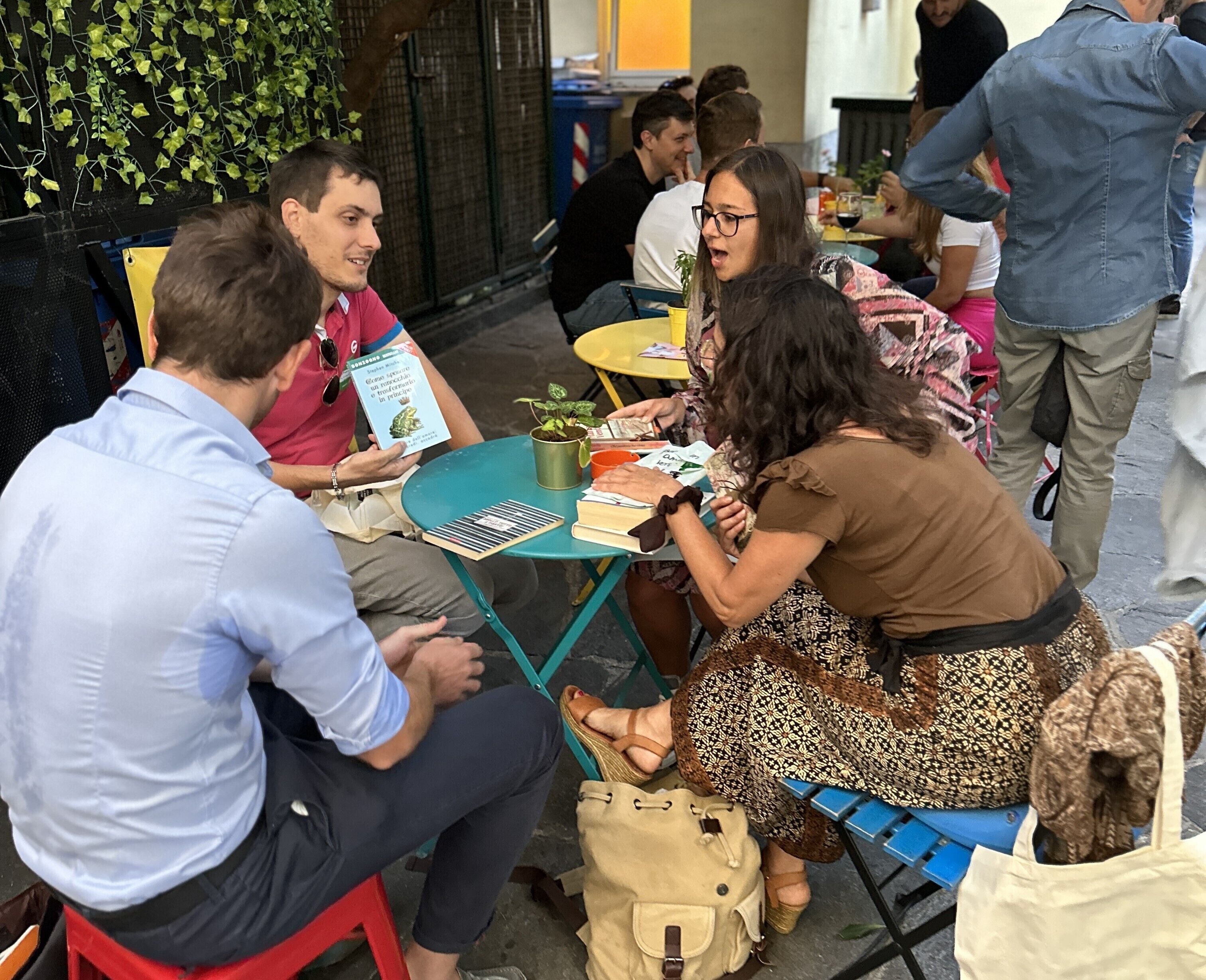 Un groupe de personnes est assis autour d’une table, sur laquelle se trouvent un livre, une plante et divers objets.
