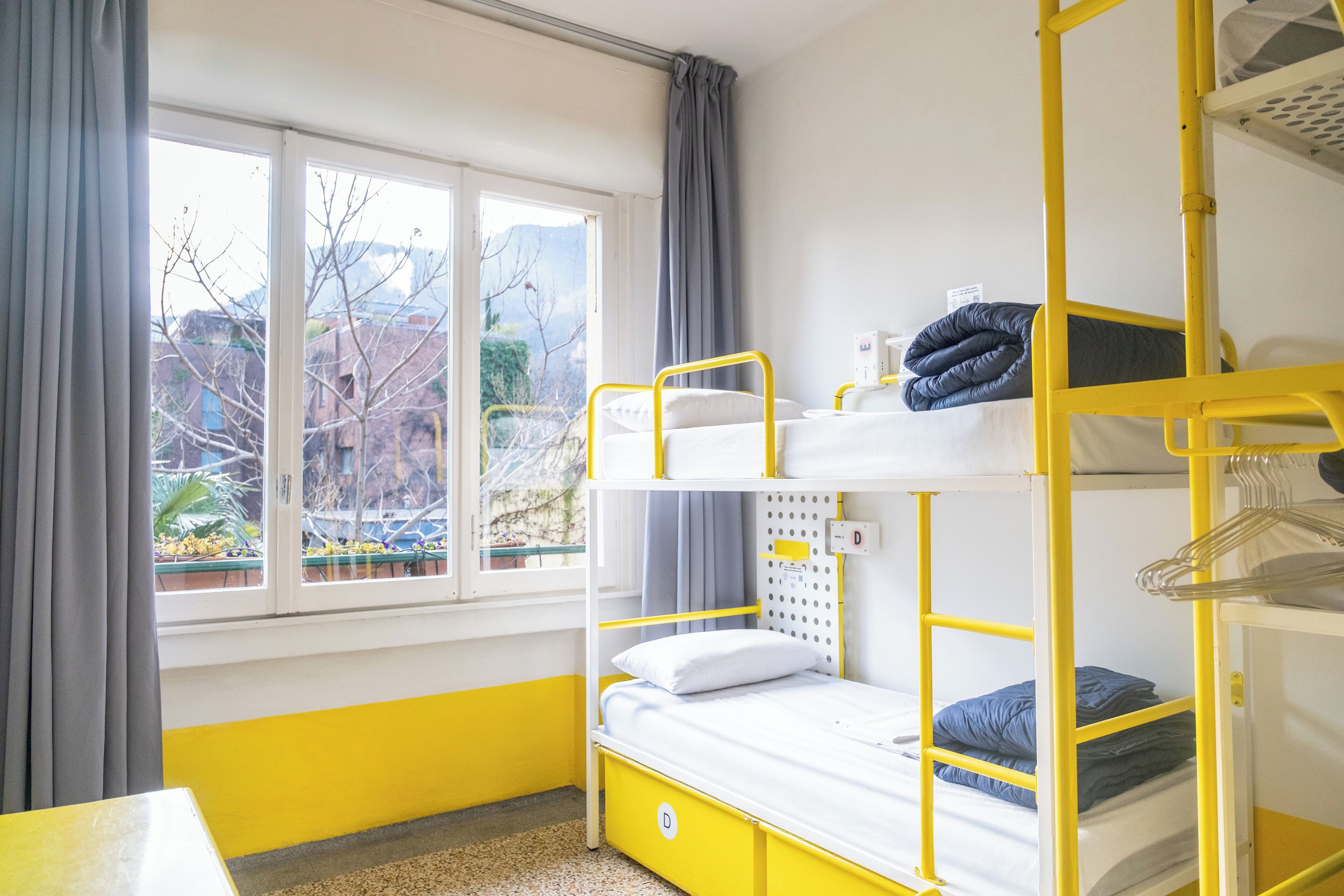 A bunk bed room with a window, curtains, and a view of buildings and trees.
