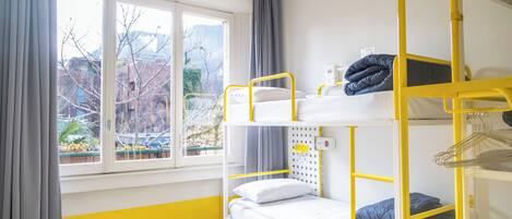 A bunk bed room with a window, curtains, and a view of buildings and trees.