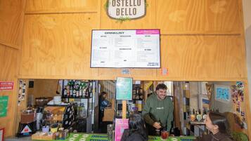 Zona de bar con interior de madera, carta de bebidas y un camarero atendiendo a un cliente.
