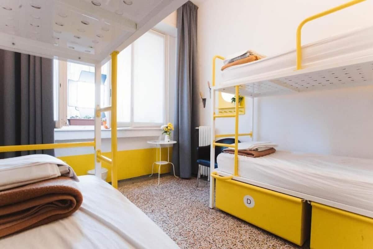 A room with bunk beds, a small table with a vase, and a window with curtains.