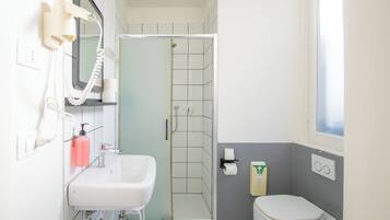 Un baño con ducha, inodoro, lavamanos y un secador de pelo montado en la pared.