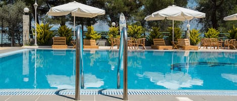 Una piscina al aire libre, sombrillas, sillones reclinables de piscina