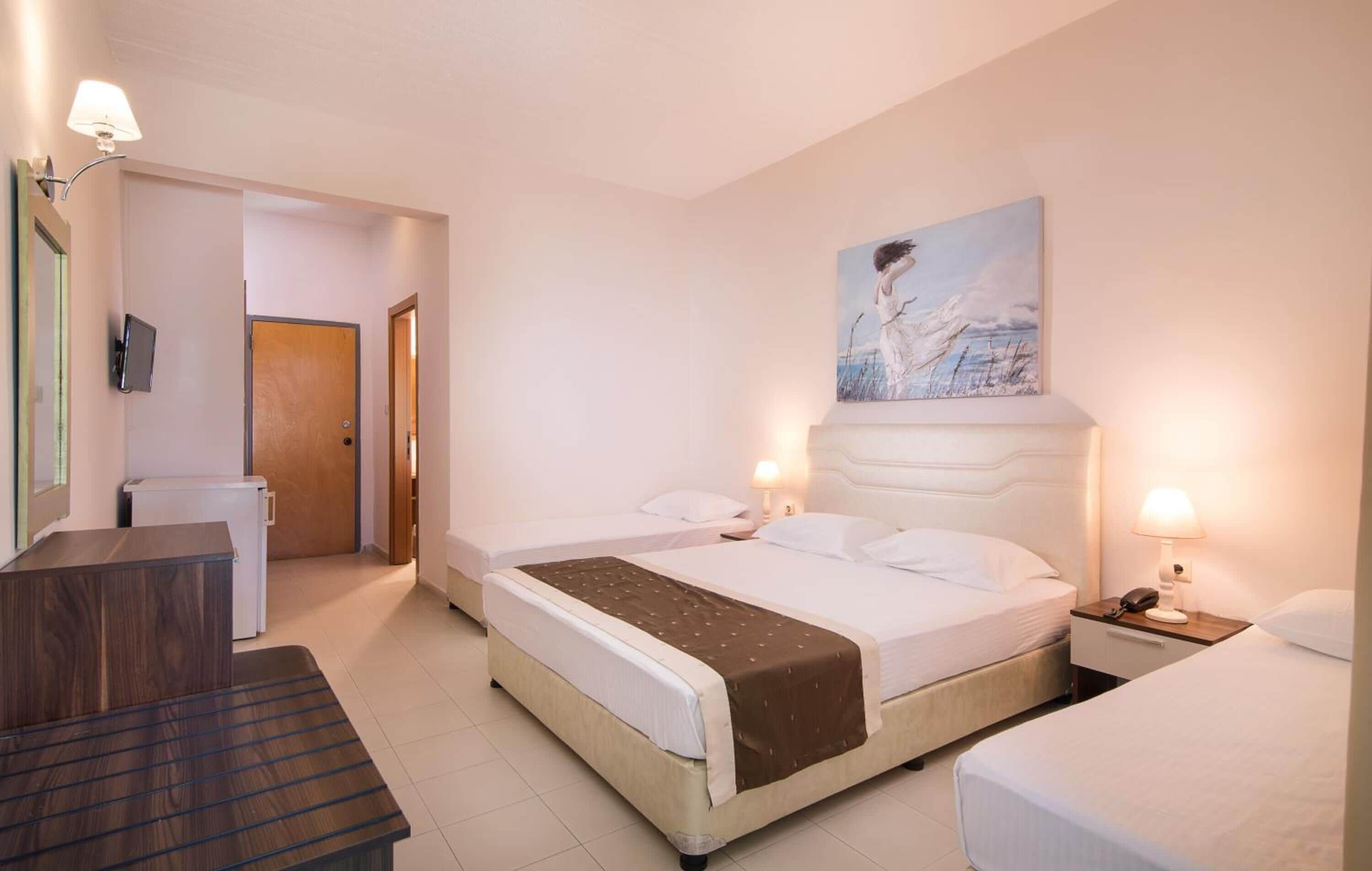 Hotelkamer met twee bedden, een bureau, een stoel, een schilderij aan de muur en een deur naar een andere kamer.