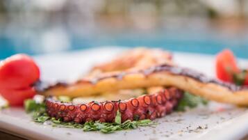 A plate with grilled octopus, garnished with herbs, and a tomato.