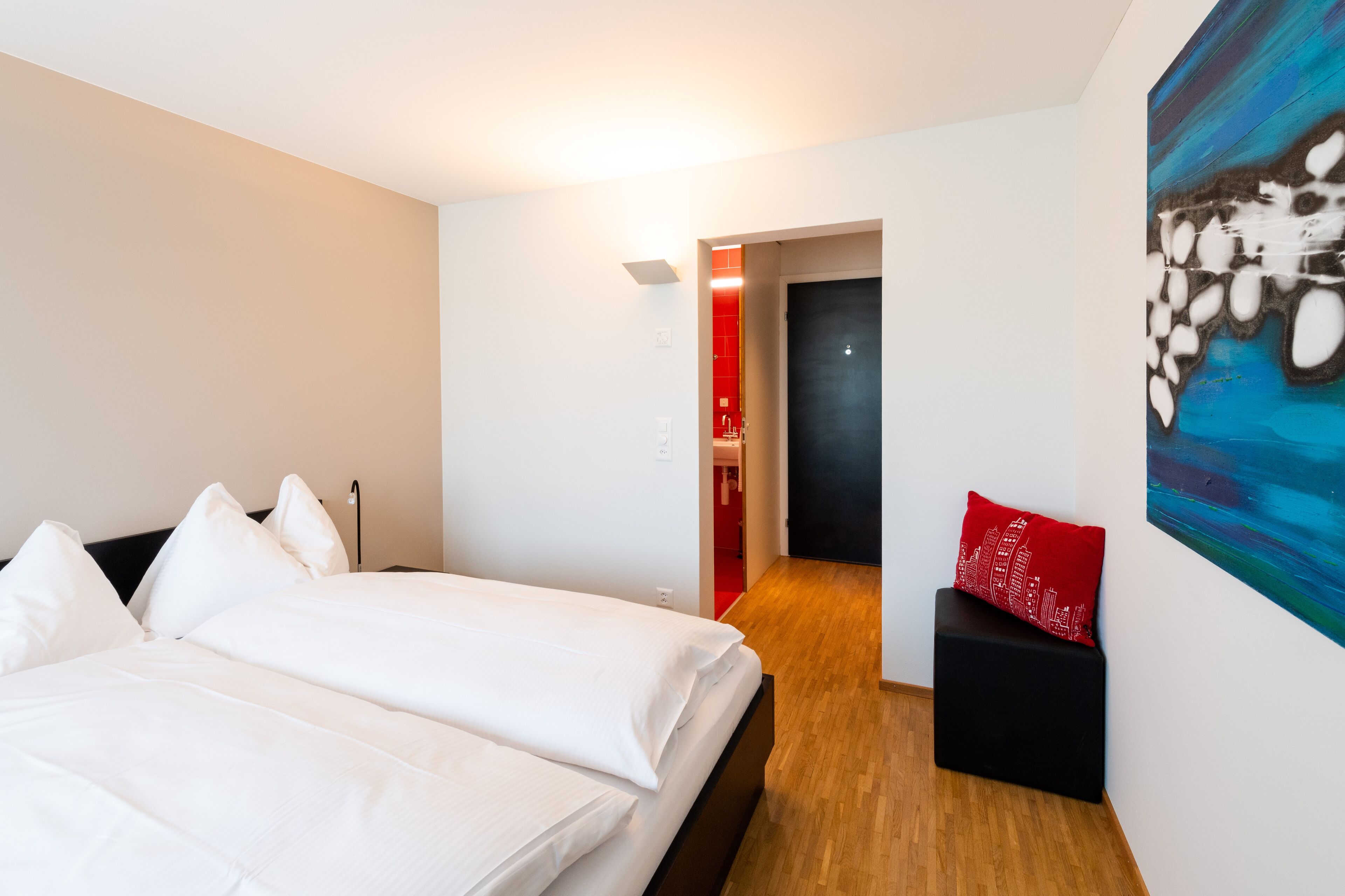 A modern hotel room with a large bed, a small seating area, and a painting on the wall.