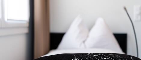 A bed with a black and white patterned pillow and white pillows.