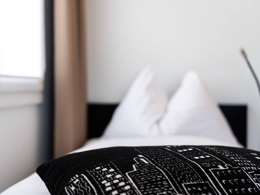 A bed with a black and white patterned pillow and white pillows.