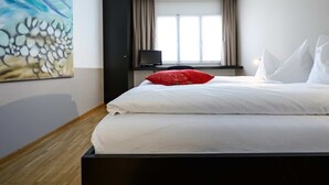 Una habitació d'hotel amb un llit, un coixí vermell, una televisió i una finestra amb cortines.