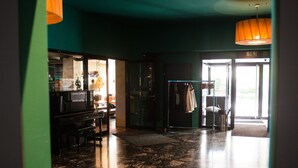 Un vestíbul amb un piano, una porta de vidre que dona a l'exterior i un penjador amb peces penjades.