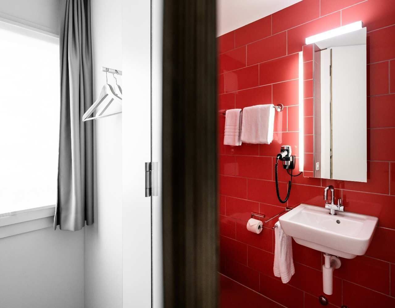 A bathroom with a red tiled wall, a white sink, a mirror, and a towel rack.