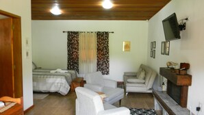 A room with a bed, two sofas, a TV, and a fireplace. - Chalés Luar da Serra (Santo Antonio do Pinhal)