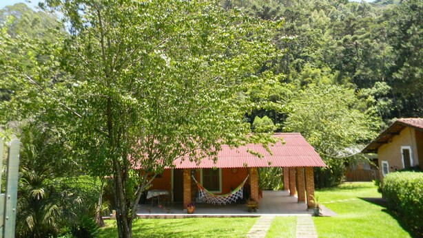 A house with a red roof, surrounded by lush greenery and a hammock. - Chalés Luar da Serra (Santo Antonio do Pinhal)