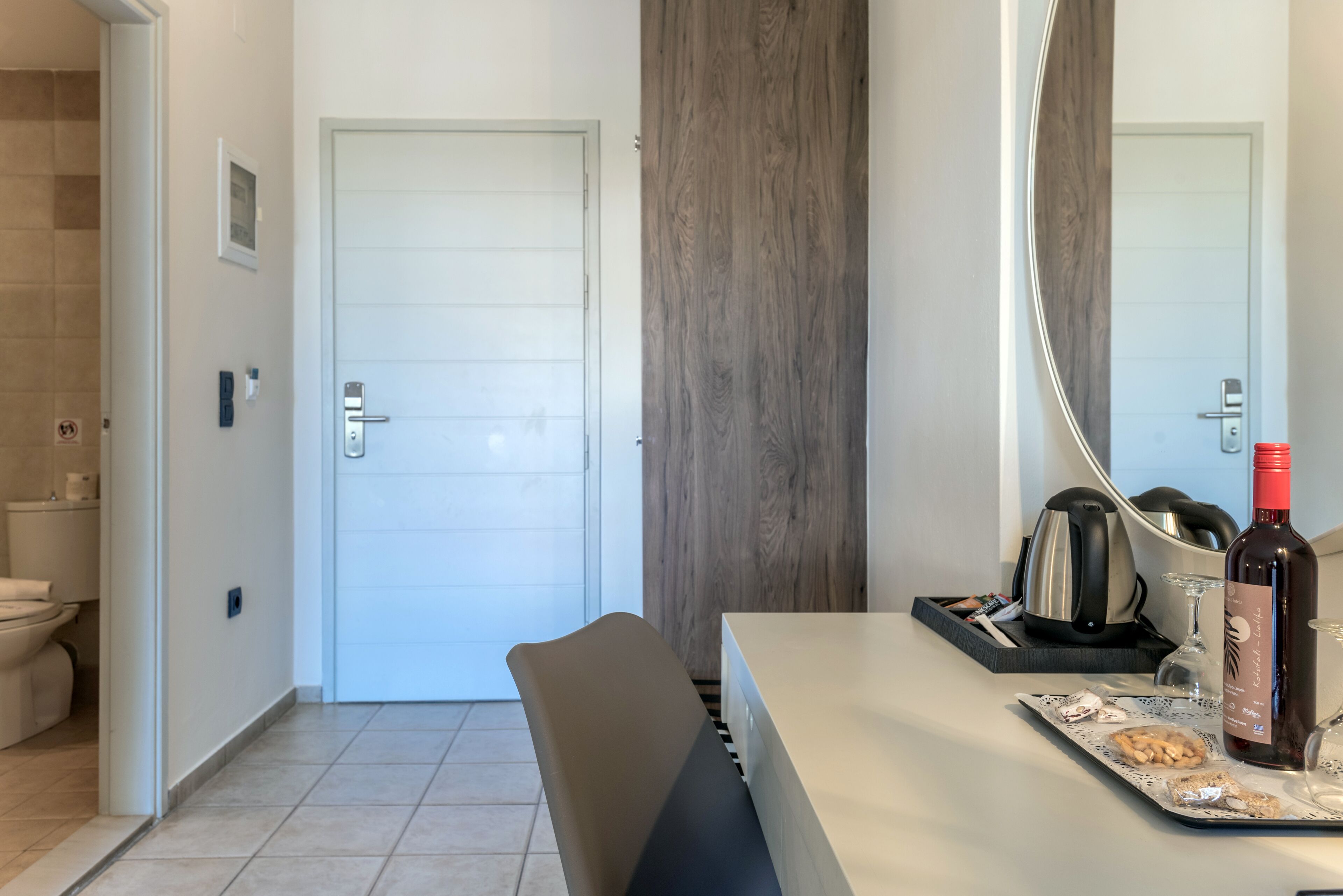 Una habitación de hotel moderna con baño, un área de comedor con mesa, sillas y una botella de vino.
