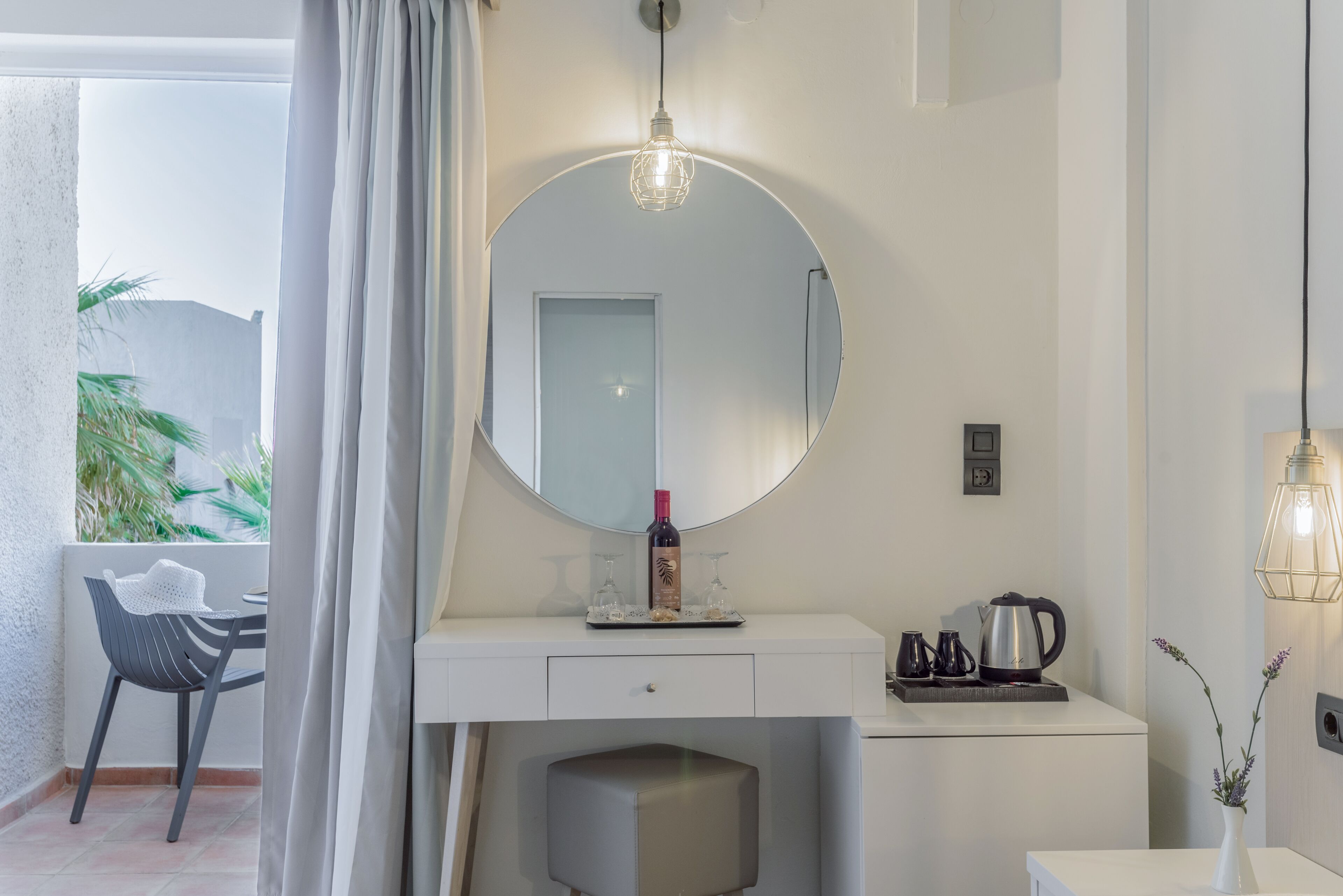Une salle de bain moderne avec un miroir rond, une bouteille de vin et une machine à café posés sur le meuble-lavabo.