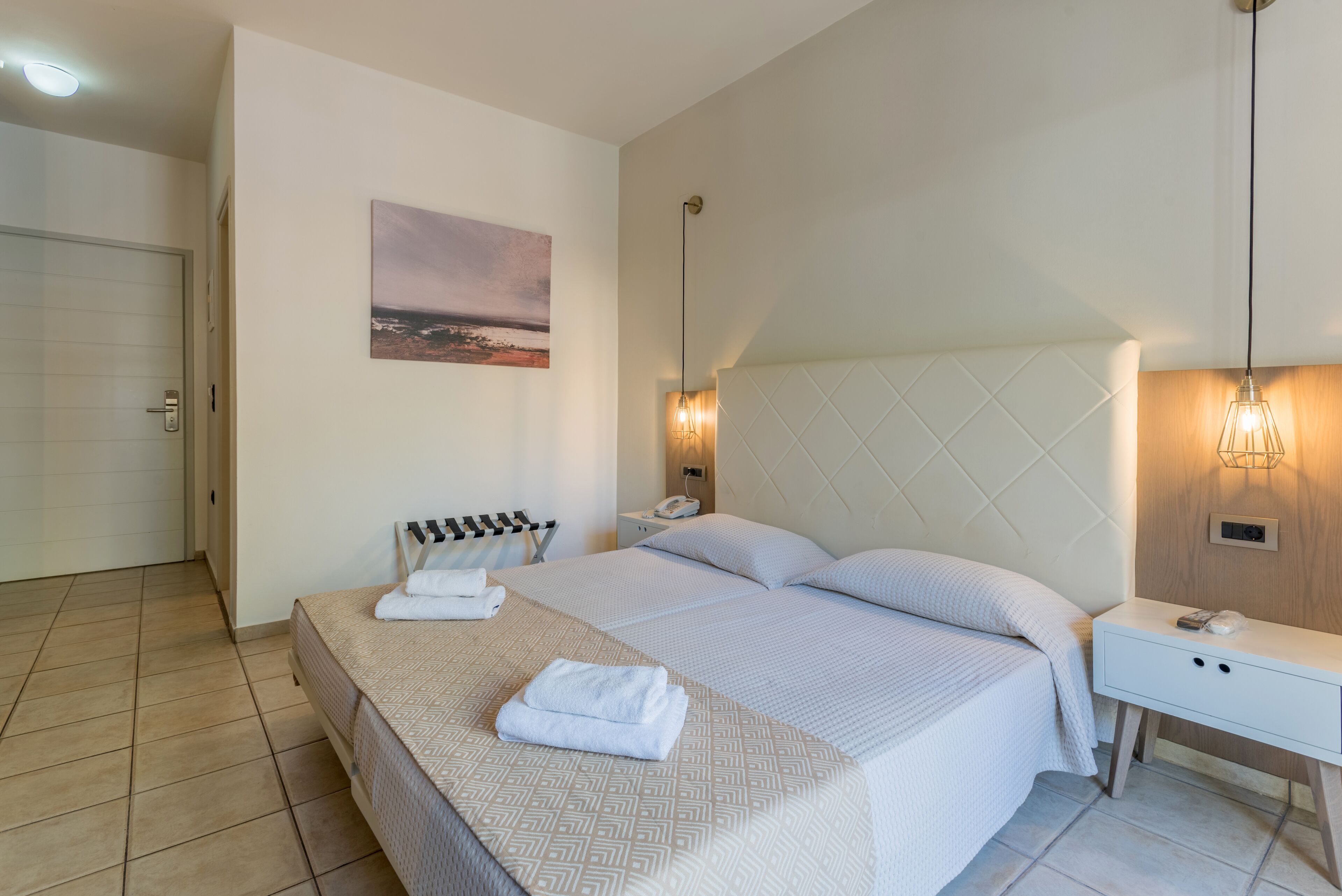 Een keurig opgemaakt slaapkamer met een bed, nachtkastjes, een wandlamp en een schilderij.