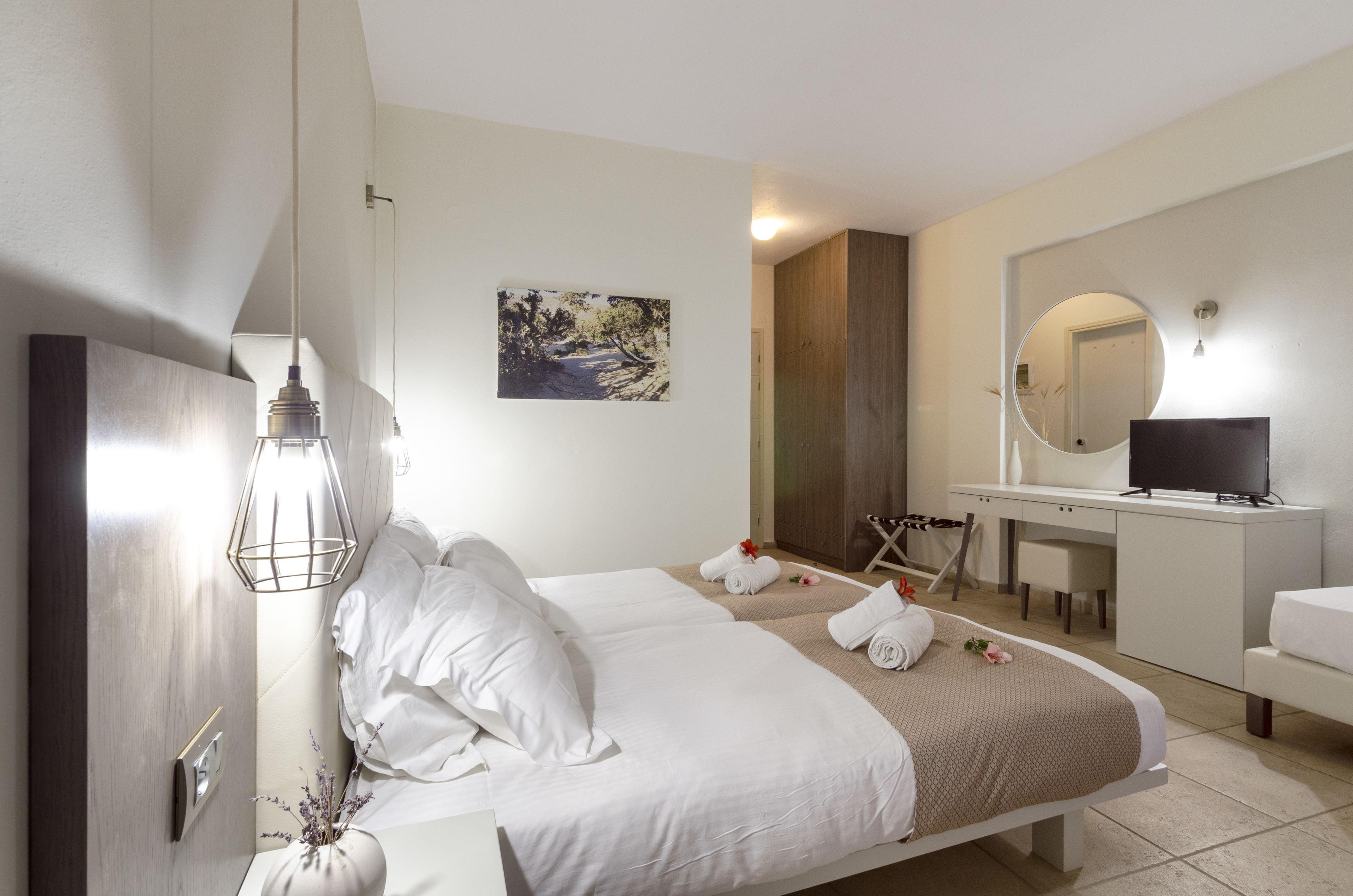 A modern hotel room with a bed, a desk, a television, and a mirror.