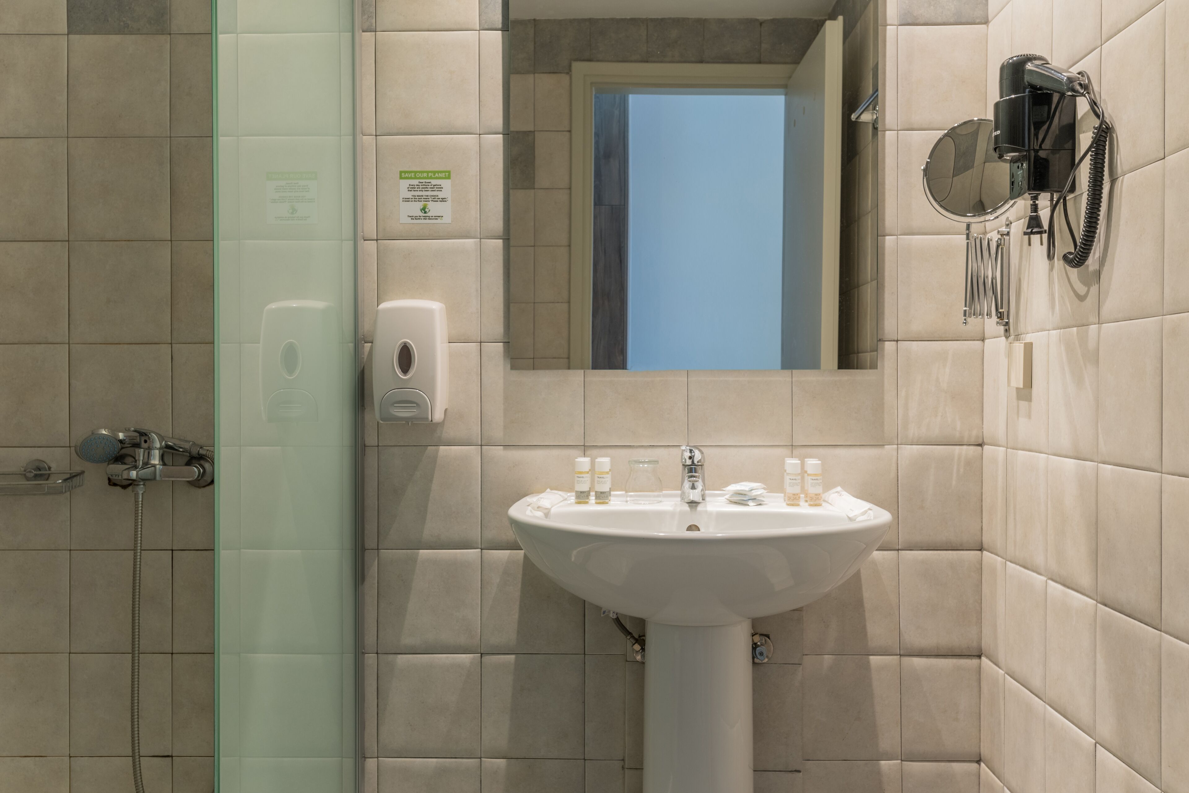 Un baño con cabina de ducha de vidrio, lavamanos con artículos de aseo y un secador de pelo montado en la pared.