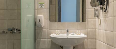 Un baño con cabina de ducha de vidrio, lavamanos con artículos de aseo y un secador de pelo montado en la pared.