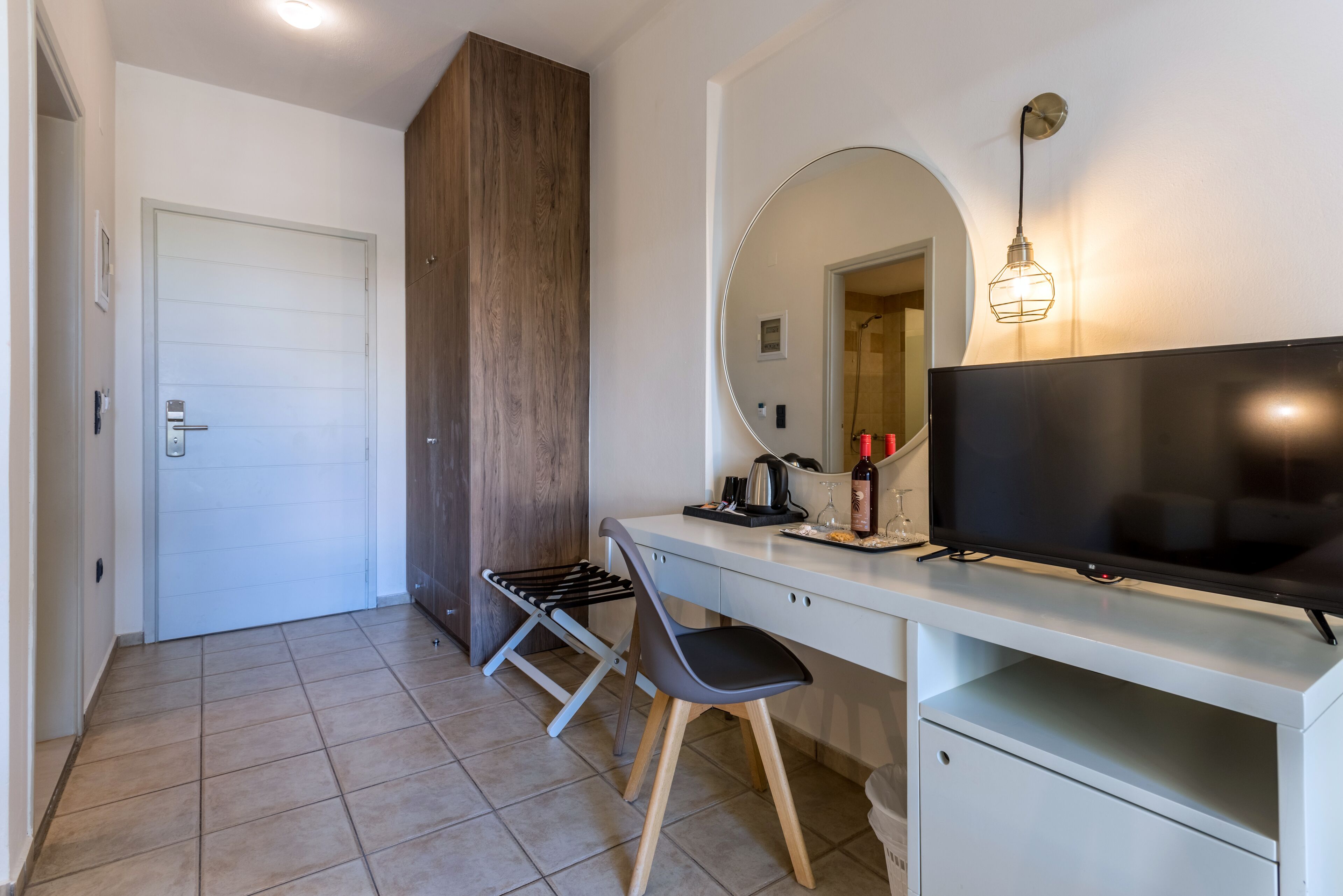 Quarto moderno com uma escrivaninha branca, uma cadeira preta, televisão, espelho e guarda-roupa de madeira.
