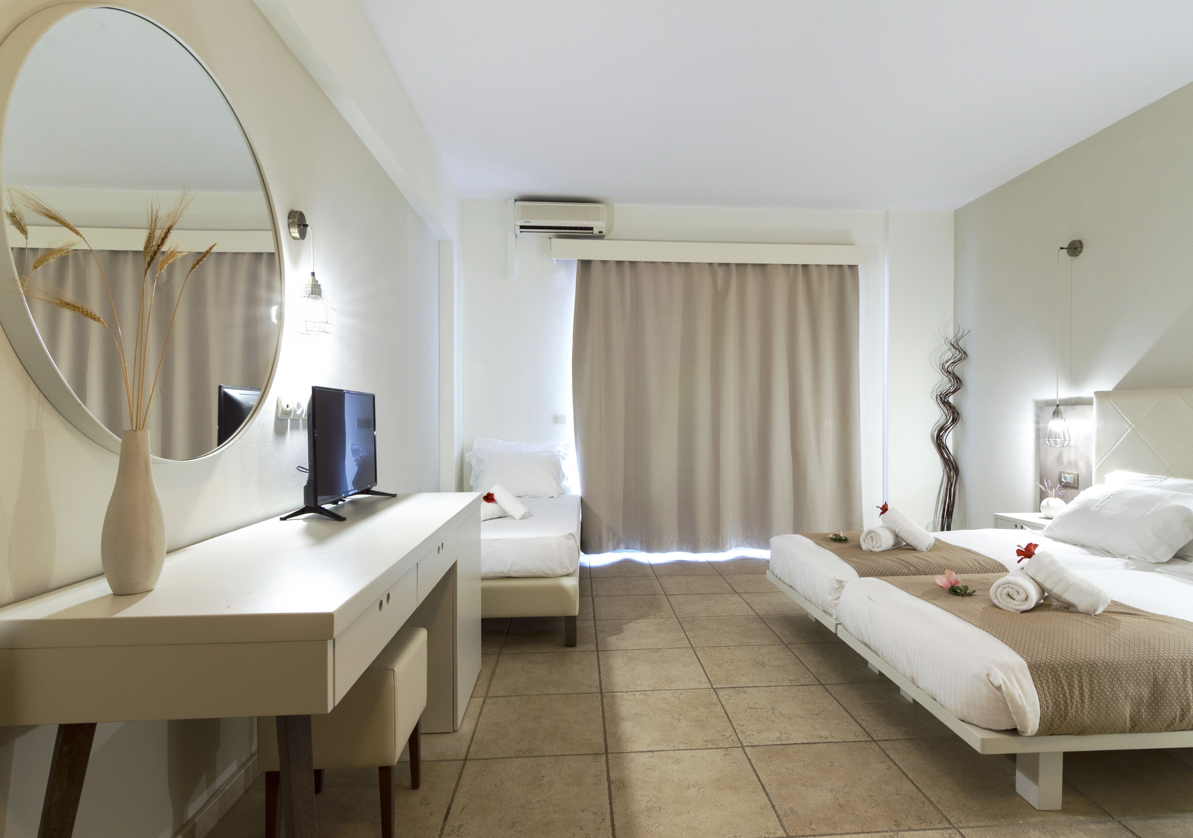 A hotel room with a bed, a desk, a chair, a mirror, and a window with curtains.