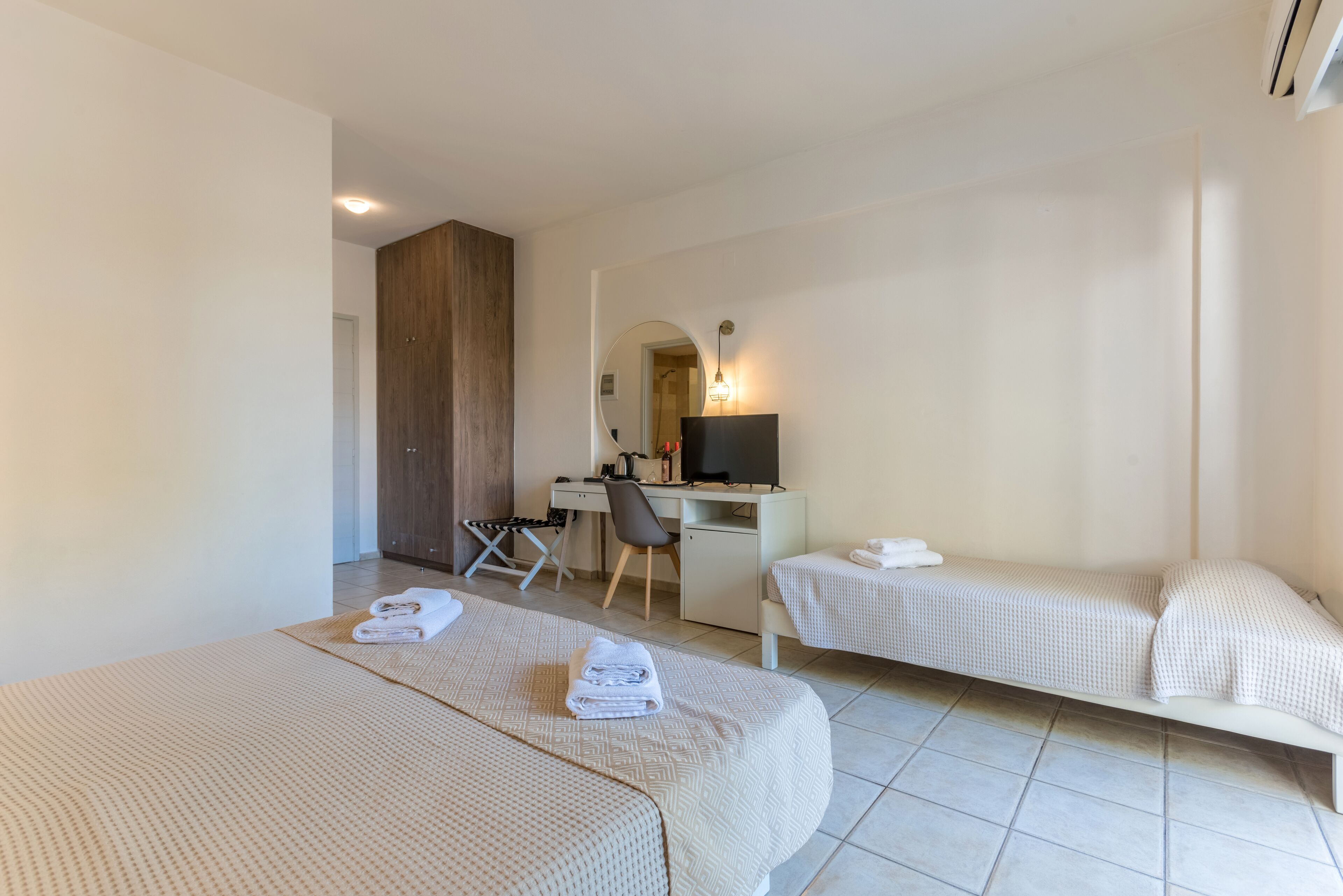 A hotel room with two beds, a desk, a chair, a TV, and a mirror.