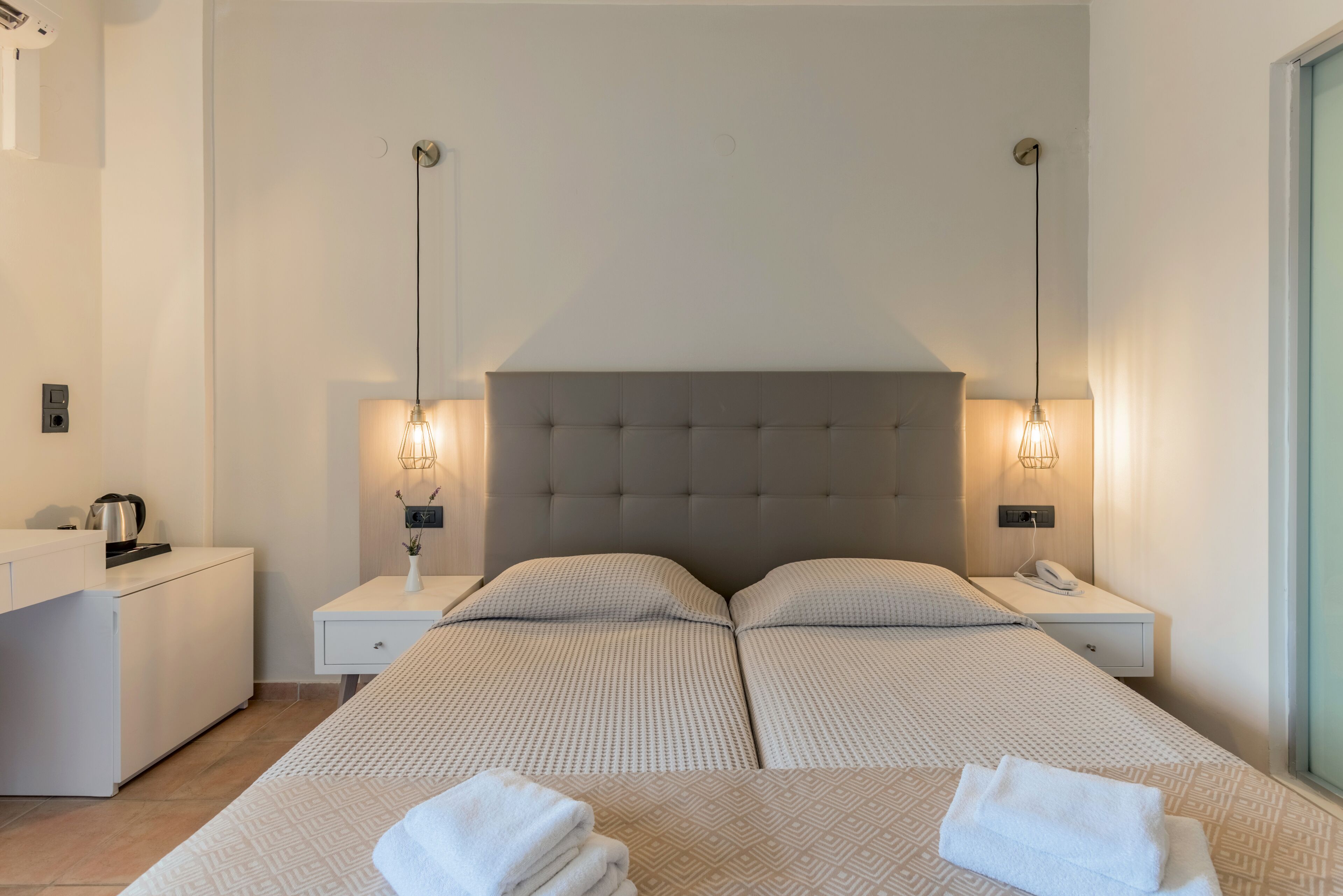 Habitación de hotel con una cama grande, dos mesitas de noche, un escritorio con un hervidor y dos lámparas de pared.