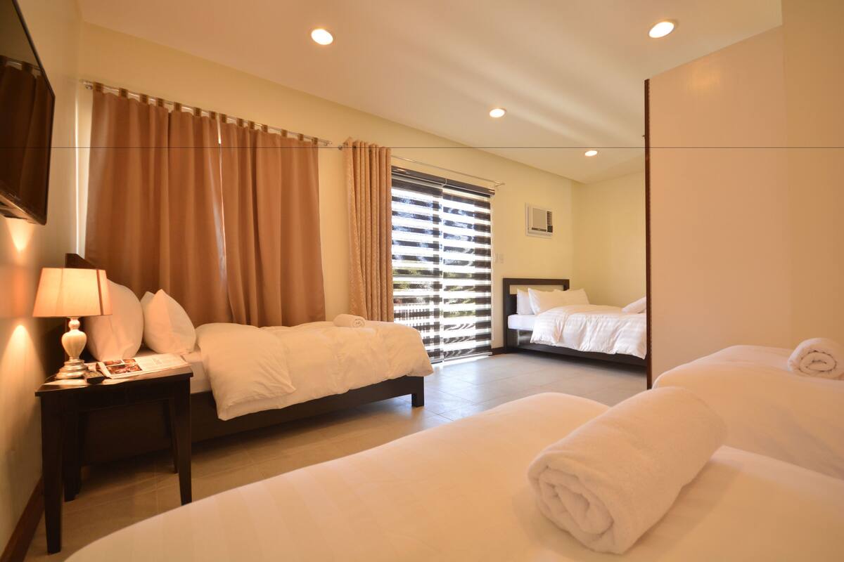 A hotel room with two beds, a nightstand with a lamp, a window with blinds, and a mirror.