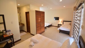 Habitación de hotel con cama, escritorio con cafetera, televisor y baño con cortina de ducha.