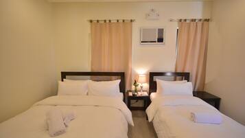 A hotel room with two beds, a nightstand with a lamp, and a wall-mounted air conditioning unit.