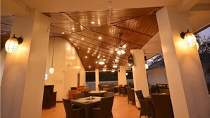 Un área de comedor al aire libre con varias mesas y sillas, techo de madera con luces colgantes y vistas al cielo.