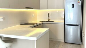 A modern kitchen with a stainless steel refrigerator, white cabinetry, and a light wood floor. - Mika Hotel (Ulaanbaatar)