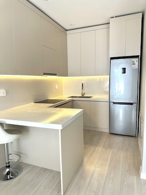 A modern kitchen with a stainless steel refrigerator, white cabinetry, and a light wood floor.