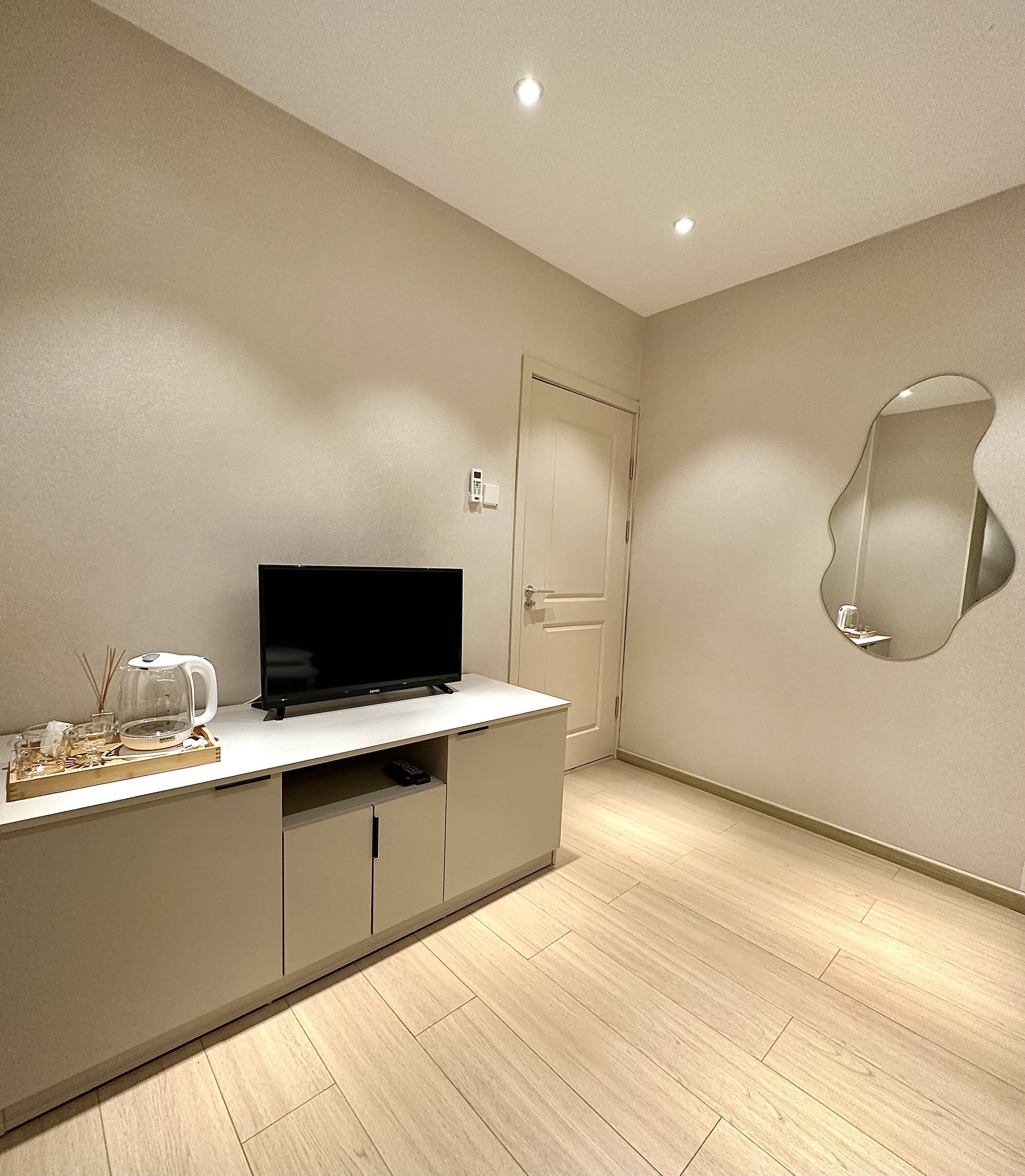 A modern living room with a flat-screen TV on a white cabinet, a door, and a wall-mounted mirror.