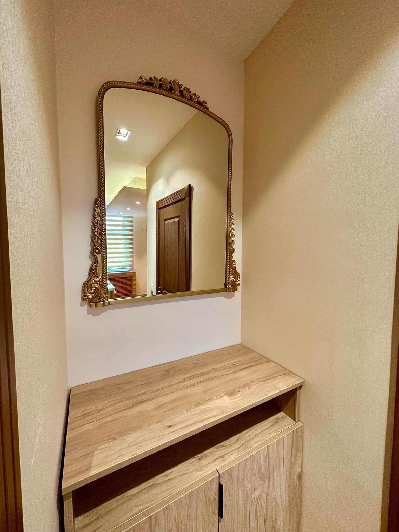 A bathroom with a wooden vanity, a large mirror with an ornate frame, and a door in the background.