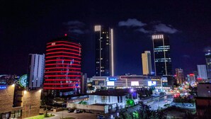 A cityscape at night with illuminated buildings, including a prominent circular building with red lights and a modern building with a sign that reads "IMAX". - Mika Hotel (Ulaanbaatar)