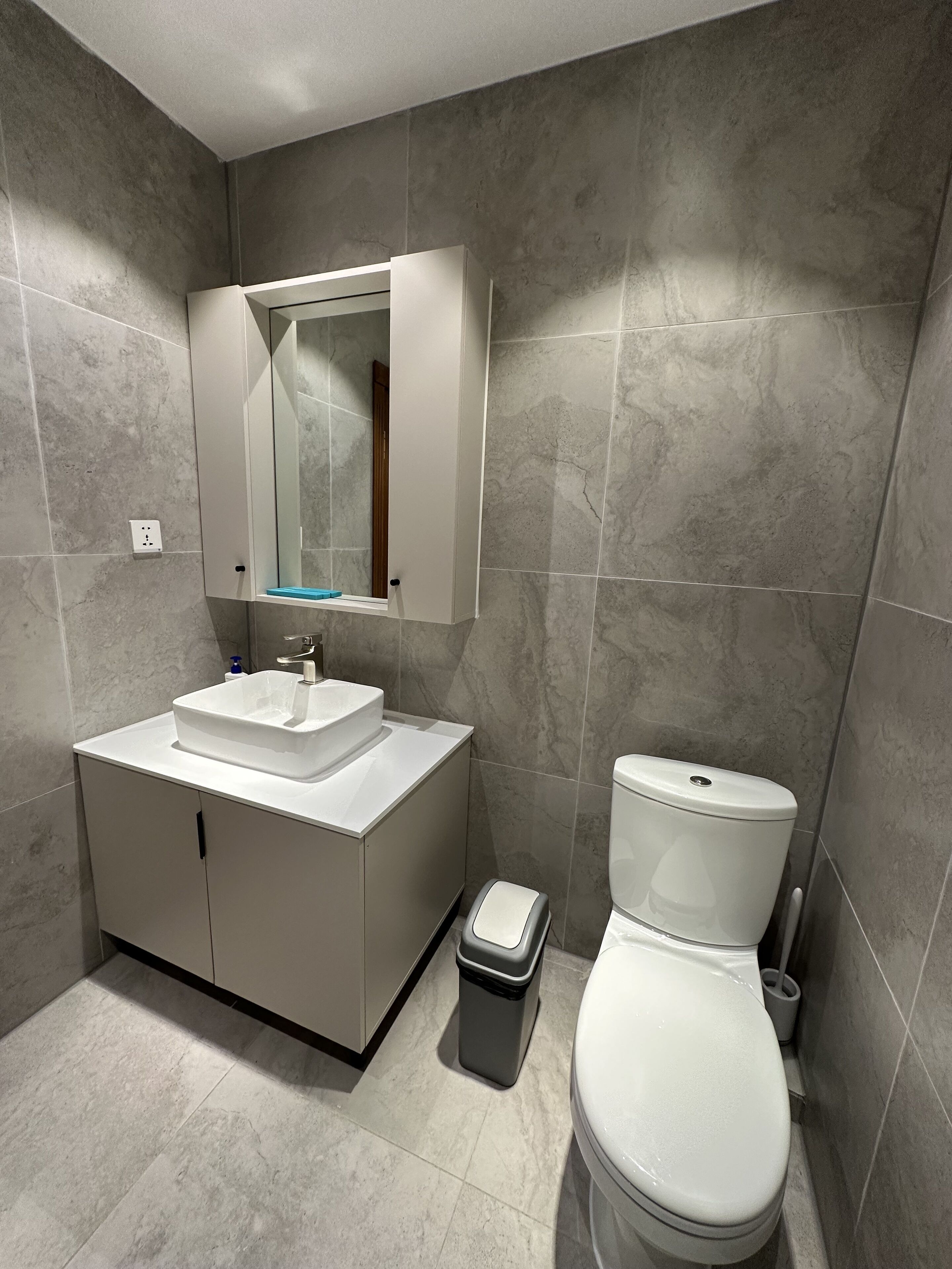 Ein modernes Badezimmer mit einem weißen Waschtisch, einem Spiegel und einer Toilette.