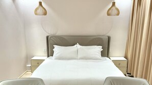 A modern hotel room with a large bed, two bedside tables, a small round table, two armchairs, and pendant lighting. - Mika Hotel (Ulaanbaatar)